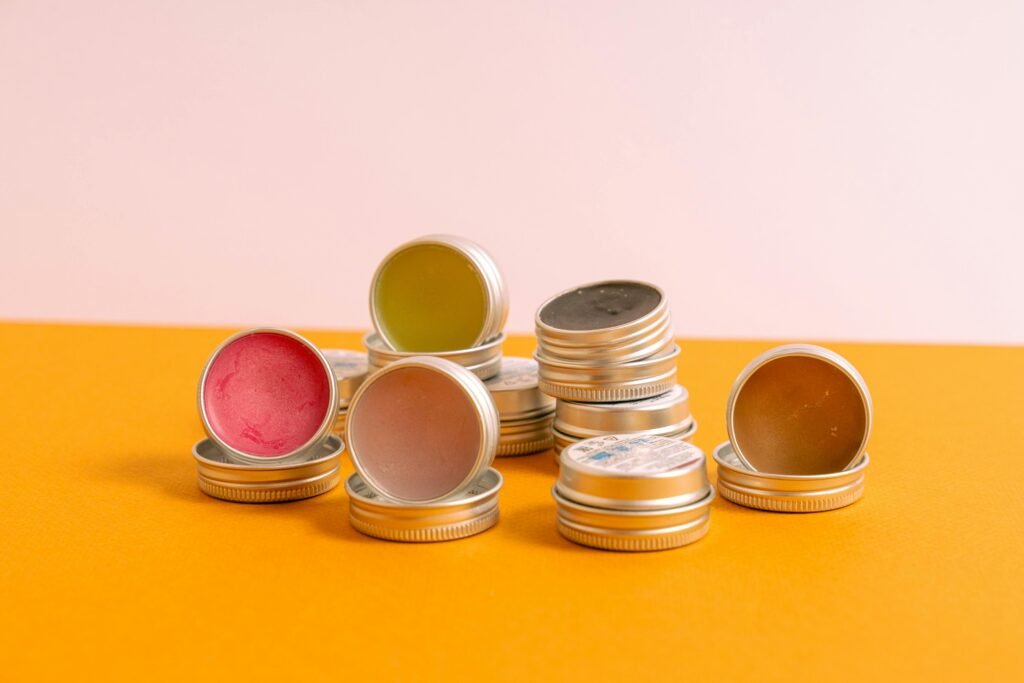 A close-up of assorted lip balms in stackable metal tins on a vibrant background.